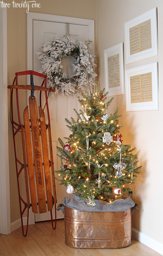 Christmas entryway with copper boiler tree stand, vintage sled, and framed vintage Christmas sheet music.