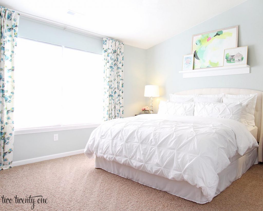 Sherwin Wiliiams Sea Salt in bedroom. Bed with upholstered headboard and white bedding. Blue and white floral curtains.