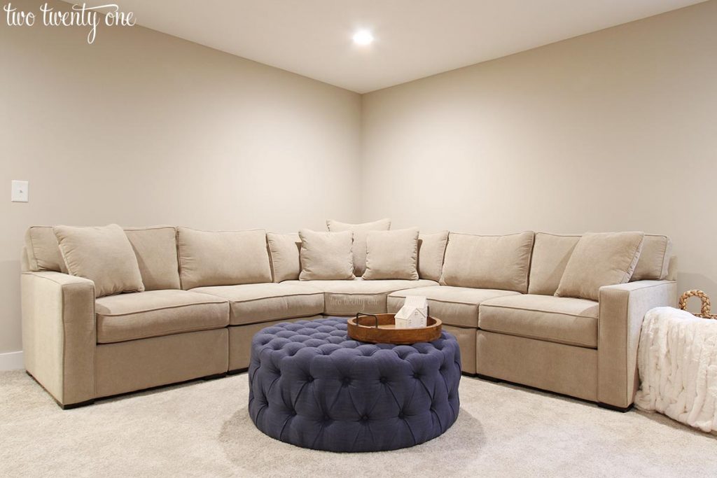 Sherwin Williams Worldly Gray in basement. Greige sectional with a tufted navy ottoman.
