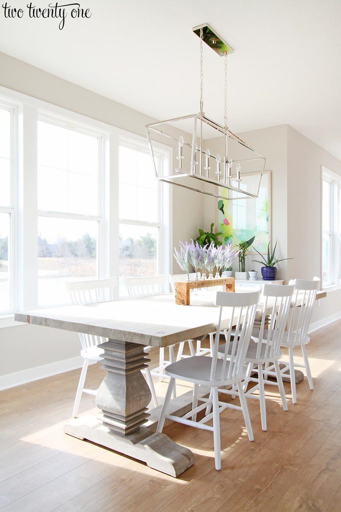 Dining room with SW Worldly Gray walls and Extra White trim. Long wooden dining room table with white chairs.