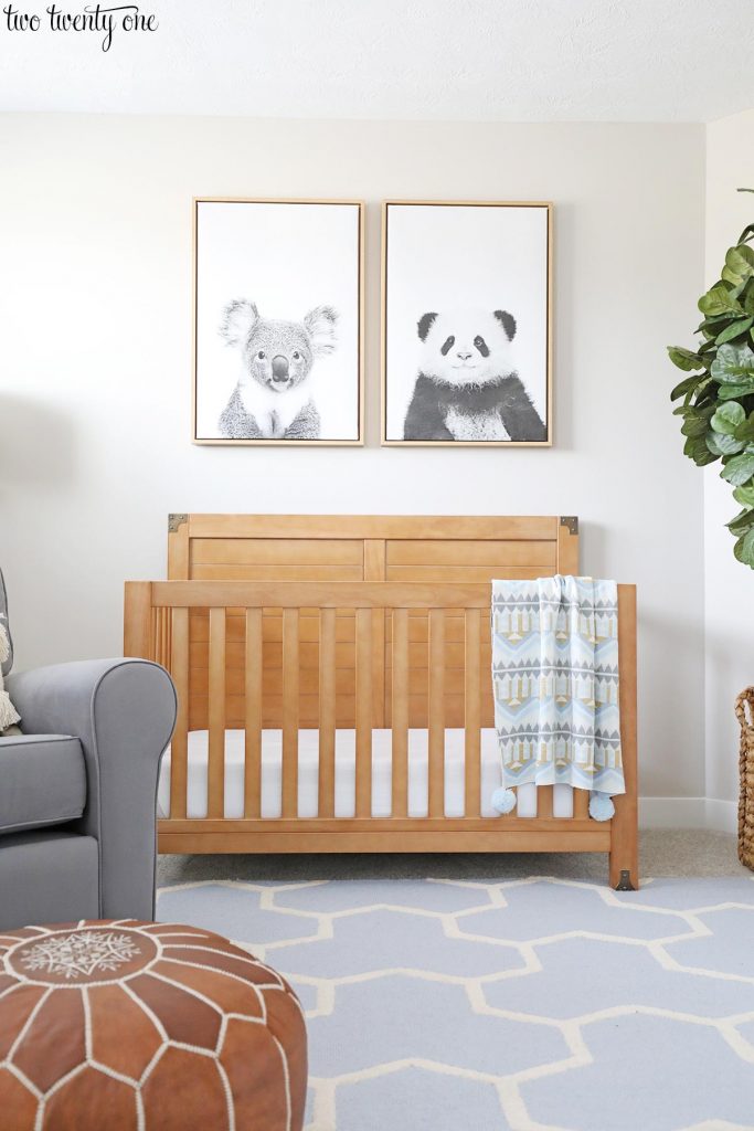 Worldly Grey nursery. Koala and panda artwork hung above a wooden crib. Blue and cream patterned rug.