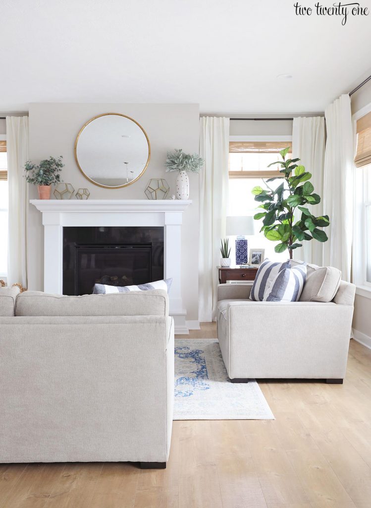 Living room with Worldly Gray walls and SW Extra White fireplace surround and trim. Greige sofas. Woven shades on the windows with white curtains.