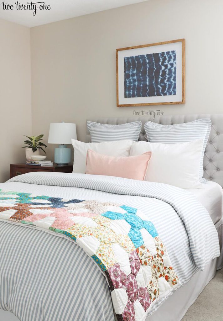 bed with vintage quilt, blue and white striped duvet, blue striped euro shams, white pillows, and light pink pillow. Shibori wall art above the bed.