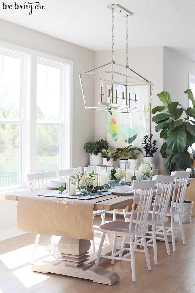 table set with blue table runner off-white candles in gold trimmer lanterns and flower arrangements of hydrangeas and greenery