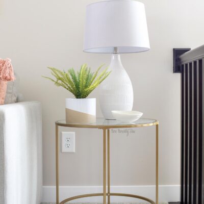 gold side table with glass top. fake plant and white lamp with gray shade on top