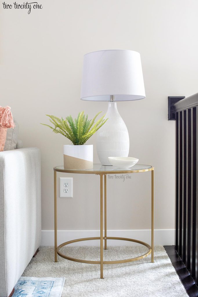 gold side table with glass top. fake plant and white lamp with gray shade on top