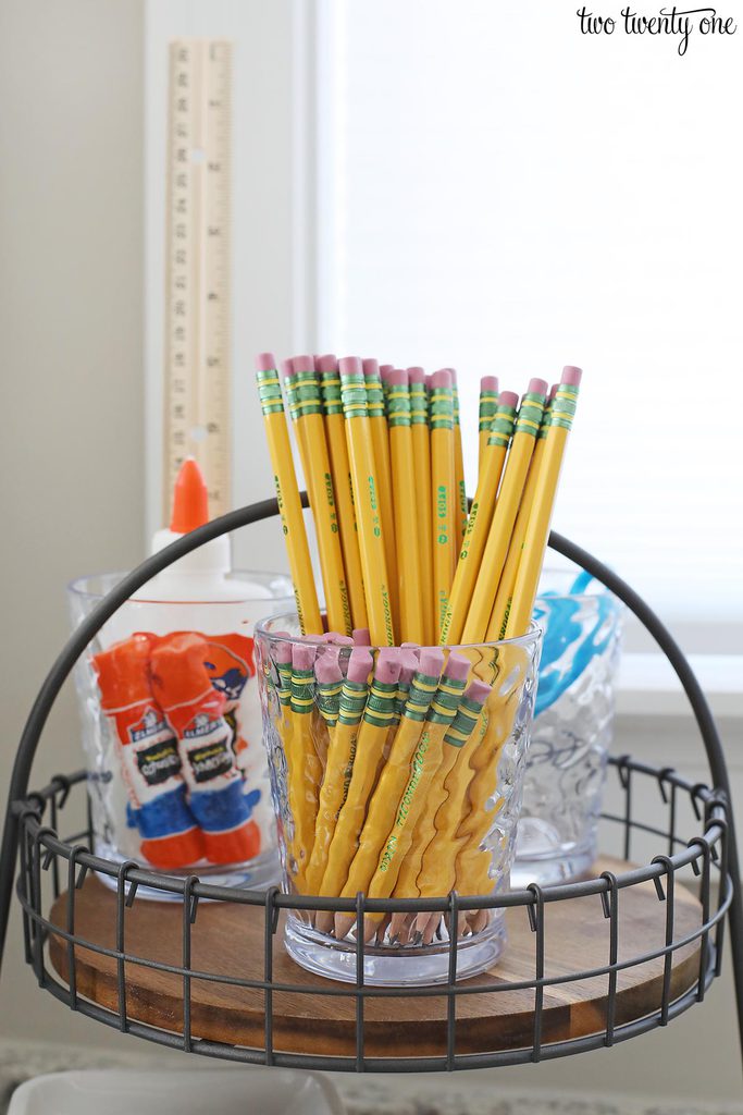 tiered wooden tray with pencils, glue sticks, and scissors in clear cups