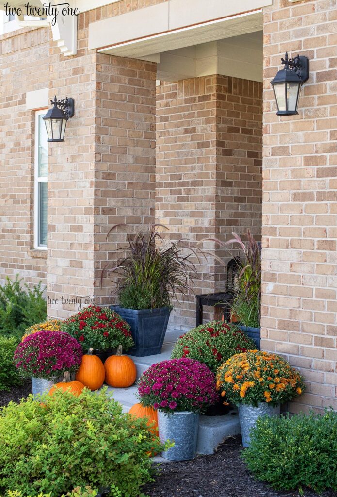 Front porch decorated for fall with mums, pumpkins, and ornamental grass.