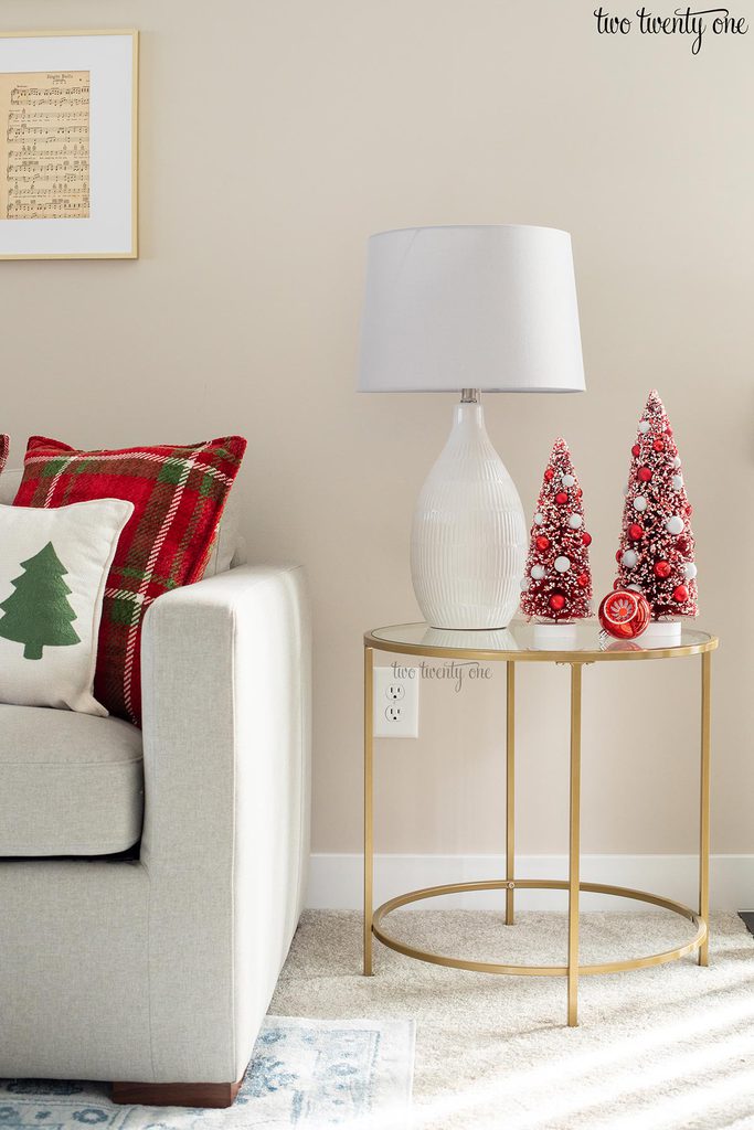 brass side table topped with a lamp and red bottle brush christmas trees