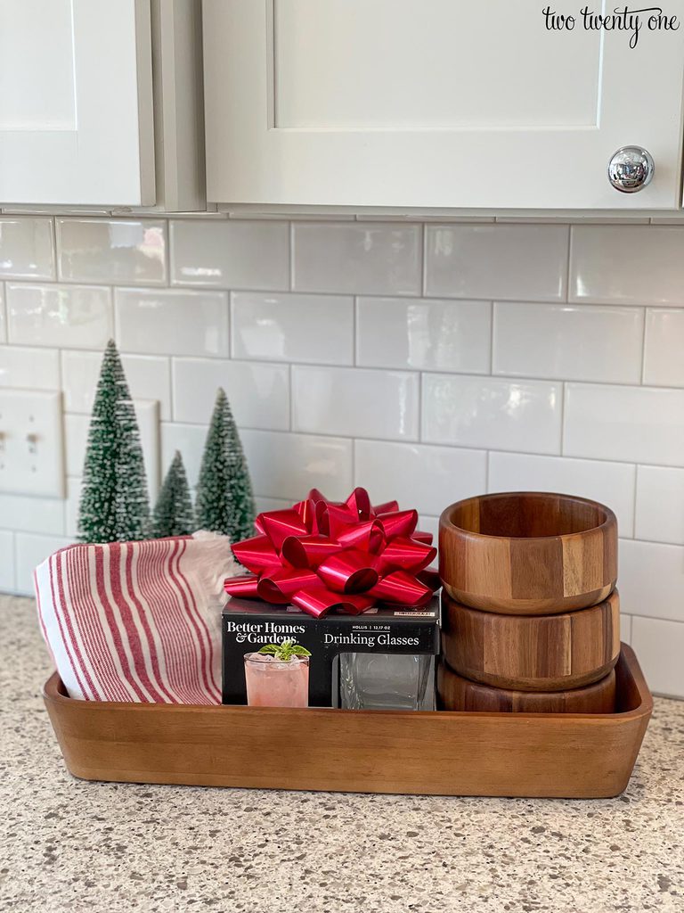 hostess gift idea made of a wooden bowl containing kitchen towels, a set of four drinking glasses, and three wooden bowls