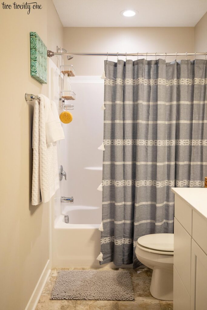 A bathroom with a white vanity, white toilet, and white tub with shower surround. A blue and white patterned shower curtain hangs in front of the shower. White towels are hung on a towel bar next to the shower.