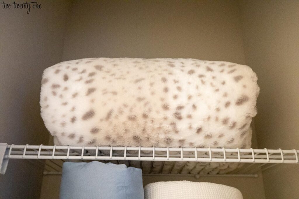 A fluffy spotted blanket on a wire shelf inside a linen closet.
