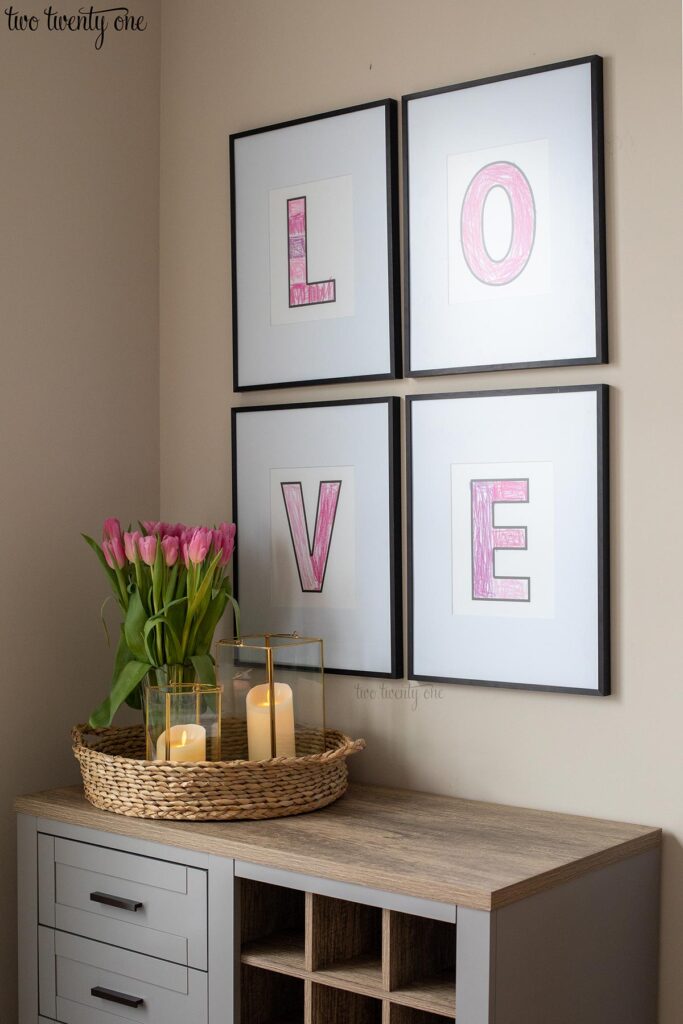 Four black frames with L, O, V, E in each frame. The frames hang above a gray bar cart.