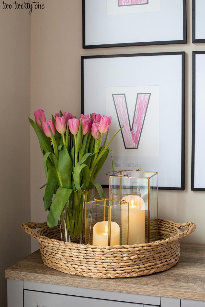 Woven basket with a vase containing pink tulips and two gold trimmed lanterns with candles in each.