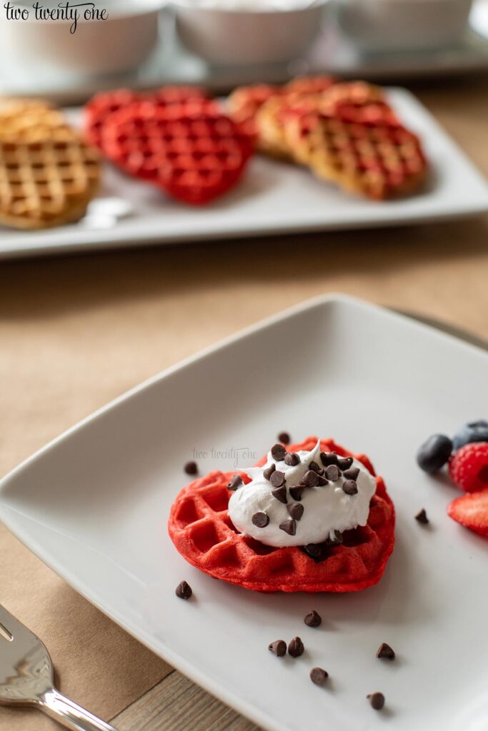 red heart shaped waffle with whipped cream and mini chocolate chips on a white plate
