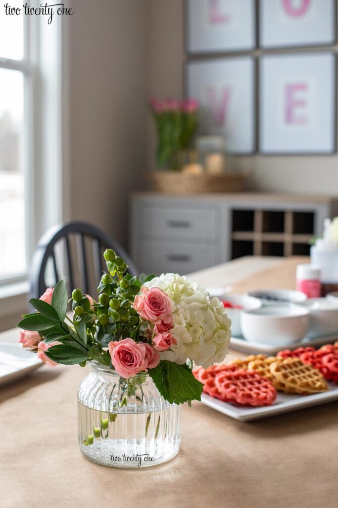 Short clear glass vase filled with a white hydrangea, pink spray roses, berries, and greenery