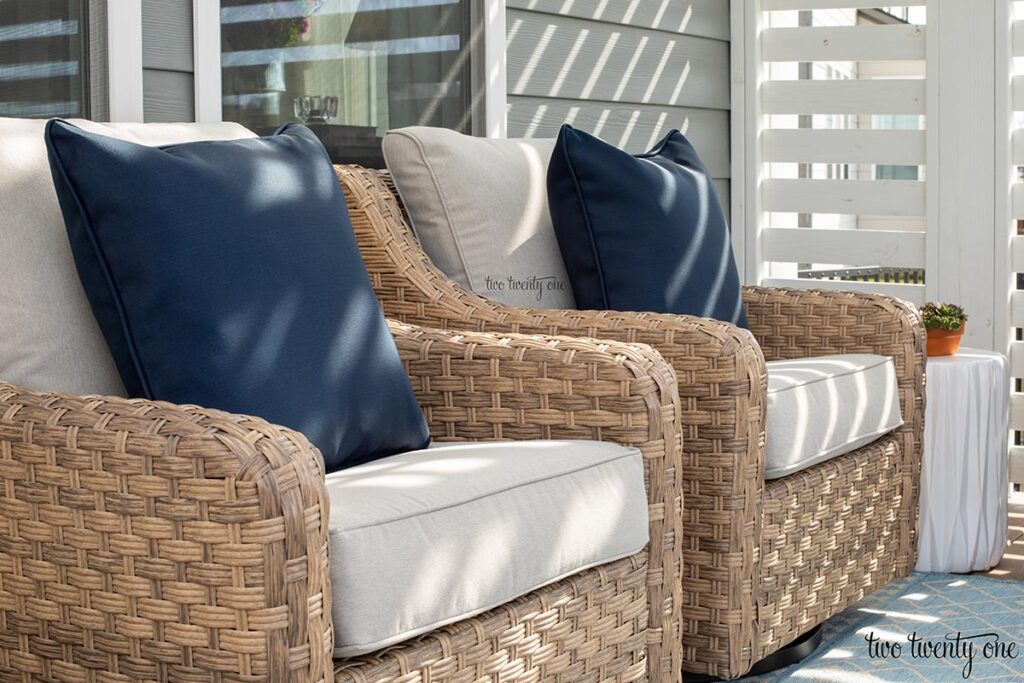 navy outdoor pillows on two wicker outdoor rocker glider chairs with light tan cushions