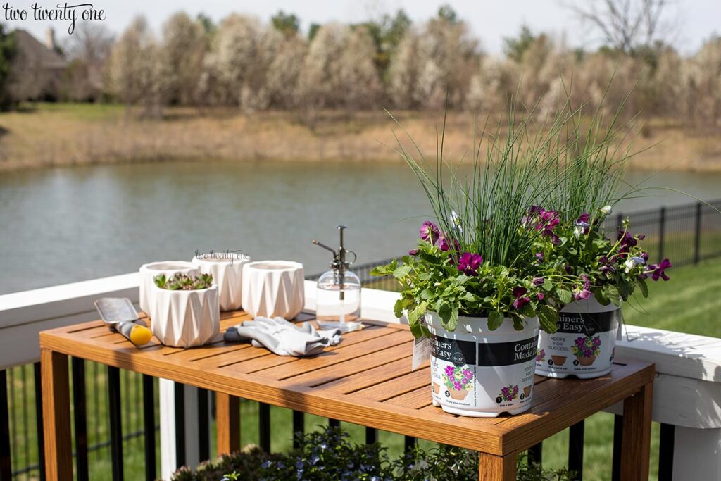 potting bench with small white planters, gardening gloves, and two flower pots on top