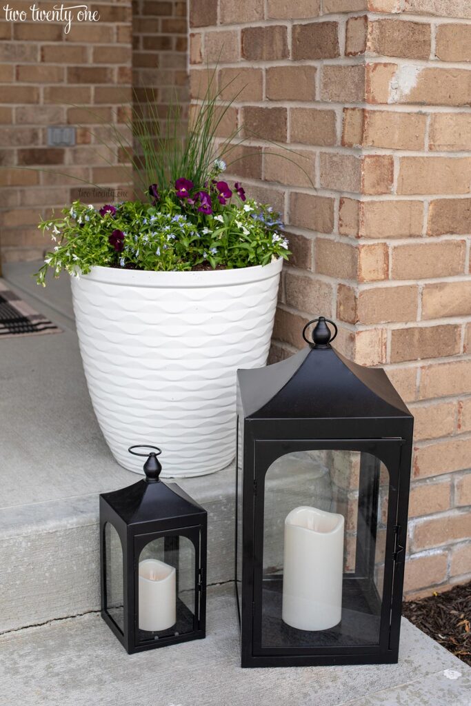 two black lanterns and a white planter with purple and white flowers