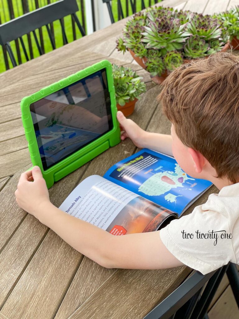 boy looking weather radar on ipad while reading weather book