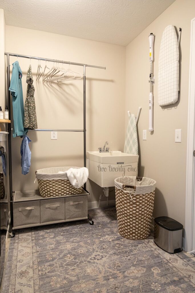 a garment rack with storage in a laundry room with the utility sink, hamper, and ironing boards on the wall