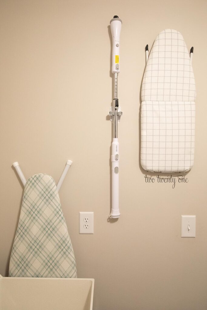 ironing board hung on wall with shower scrubber also hung on the wall large ironing board leaning against wall