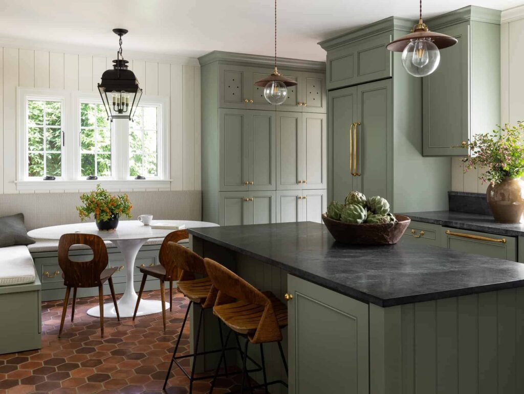 Kitchen with off-white walls and muted green painted cabinets. Counterops are soapstone and the floor is terra cotta hexagon tiles.