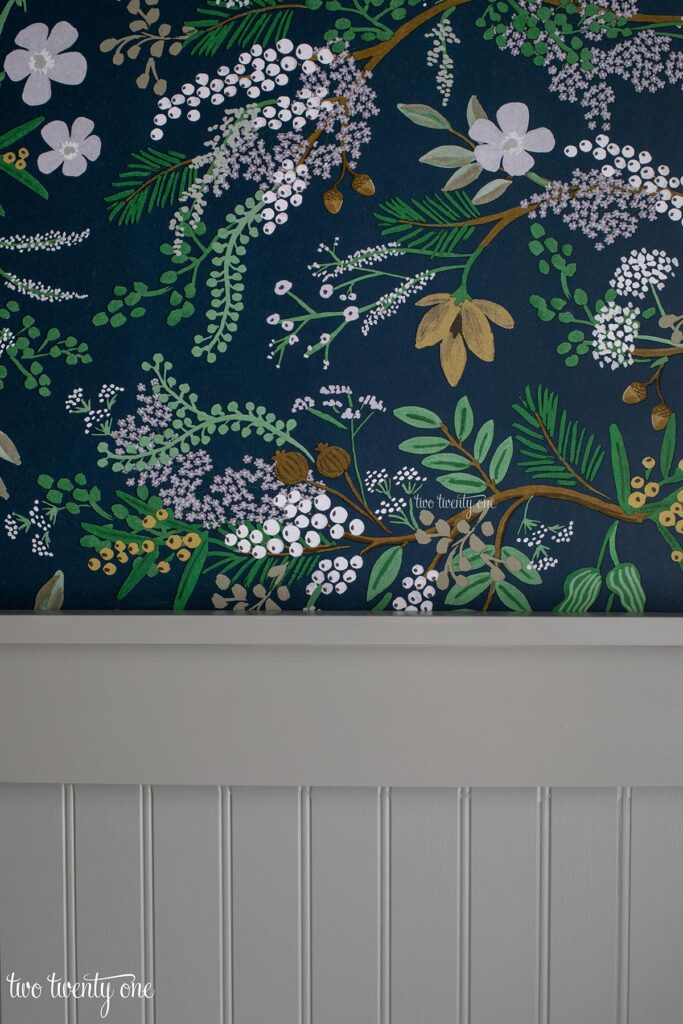 Muted green paint on beadboard paneling in a bathroom with botanical wallpaper above the paneling. 