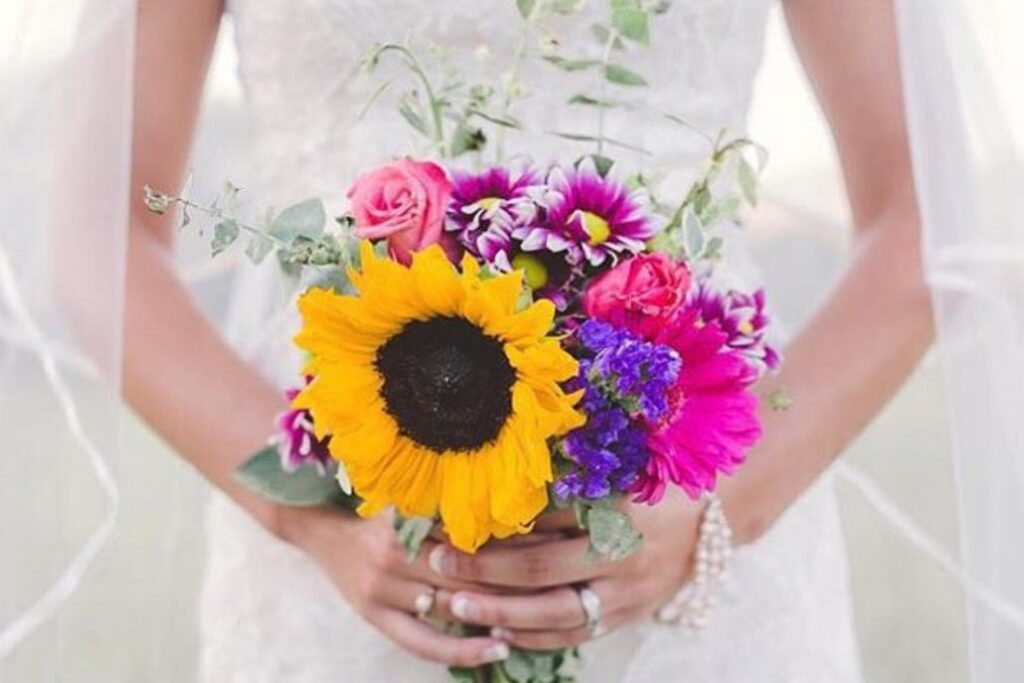 Wedding bouquet made with sunflowers, roses and other pink and purple flowers.